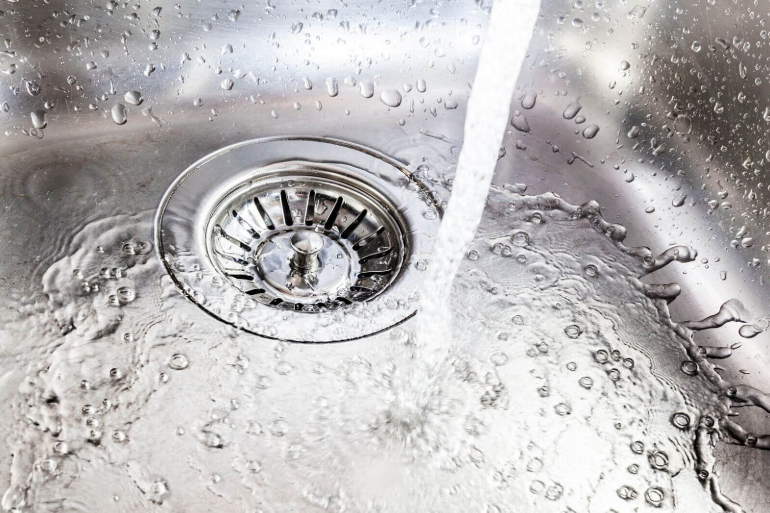 Running water flowing into a stainless steel kitchen sink drain