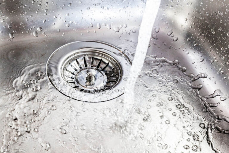 Running water flowing into a stainless steel kitchen sink drain